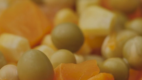 Peas, corn and cooked carrots seen in a very close shot.