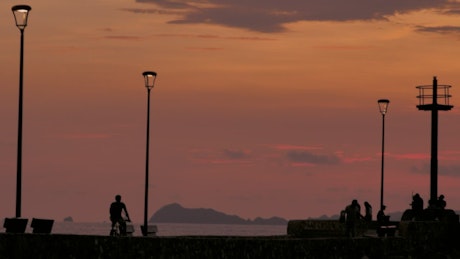 Pedestrians on a beach pier in the sunset.