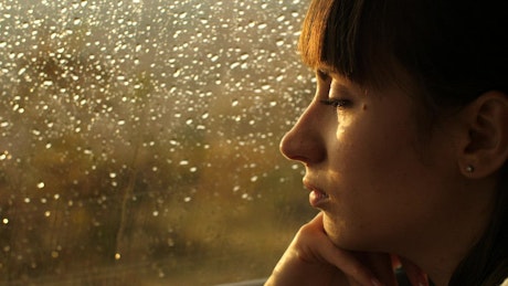 Pensive woman looking out of a window on a rainy day