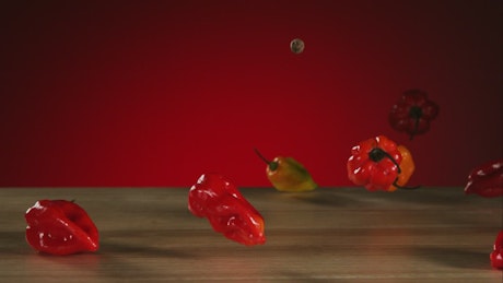Peppers falling and bouncing on a wooden table