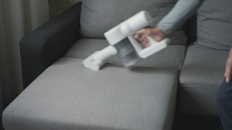 Person cleaning the couch with a handheld vaccum.