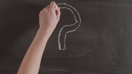 Person drawing a large question mark with chalk on a blackboard.