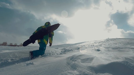 Person hiking through deep snow with their snowboard.