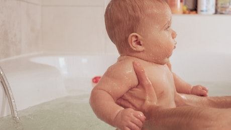 Person holding baby in bathtub with both hands.