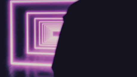 Person in the dark in front of a square tunnel of neon lights