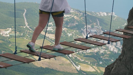 Person on a suspension bridge between mountains.