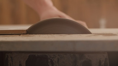 Person shaping ceramic tiles on a grinder.