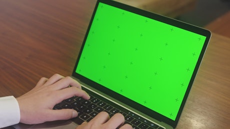Person typing on a laptop with a green screen.