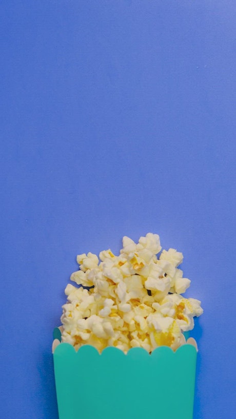 Popcorn scattered in stop motion on a blue background.