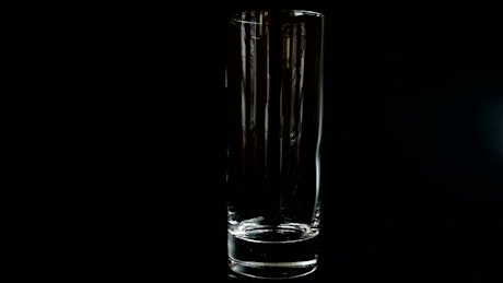 Pouring ice and lemonade into a glass on black background