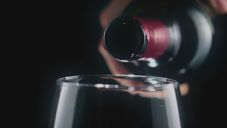 Pouring red wine from a bottle, very close view.