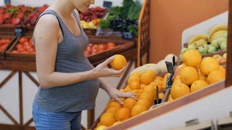 Pregnant woman buying fresh oranges at the market