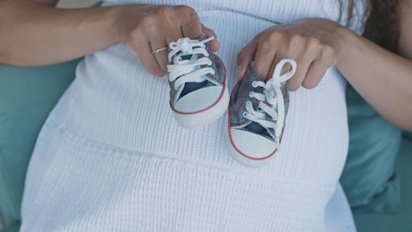Pregnant woman holding small baby shoes, top shot.