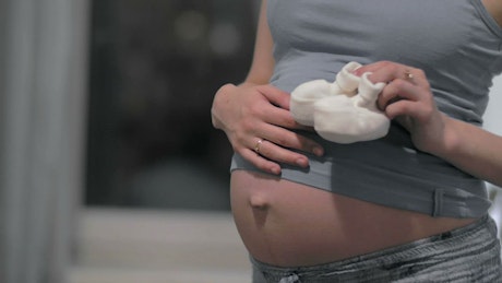 Pregnant woman holding white shoes.