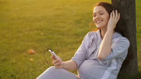 Pregnant woman listening to music on her cell phone.