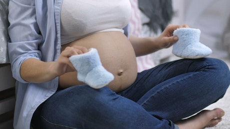 Pregnant woman playing with small baby shoes