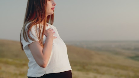Pregnant women standing on a hill practicing her breathing.
