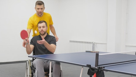 Professional ping pong player trains athlete with leg disabilities.