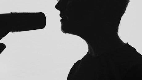 Profile silhouette of a man singing into a microphone.