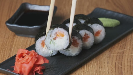 Putting sushi on a wooden table with chopsticks.