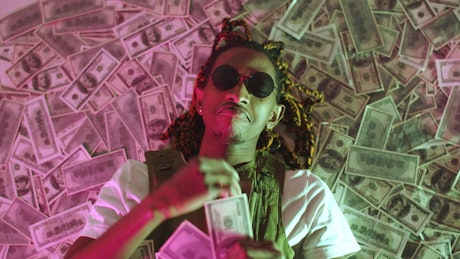 Rapper lying in a pile of money throwing money in the air.