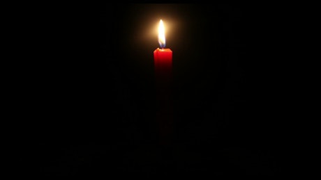 Red candle burning in a dark room.