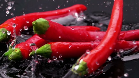 Red chili pepper falling into black water.