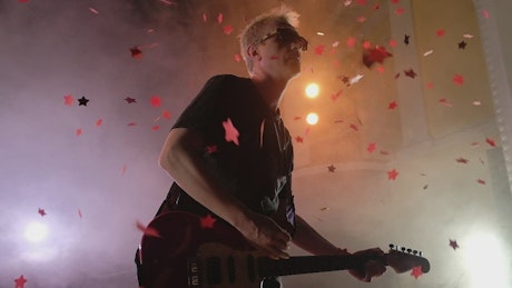 Red confetti stars fall on performing guitarist.