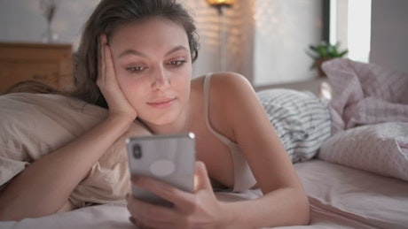 Relaxed woman on bed looking at her smartphone.