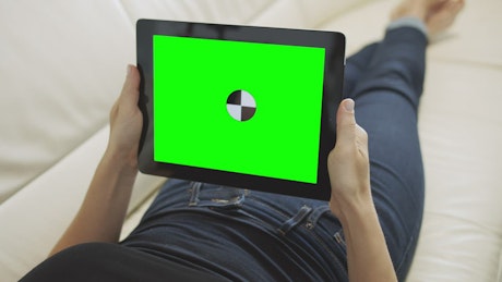 Relaxing on sofa holding greenscreen tablet with chroma key
