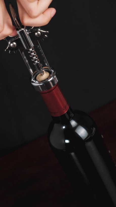 Removing the cork from a wine bottle with a corkscrew.