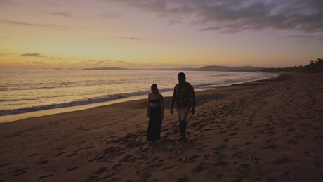 Romantic couple walk along a beach at sunset.