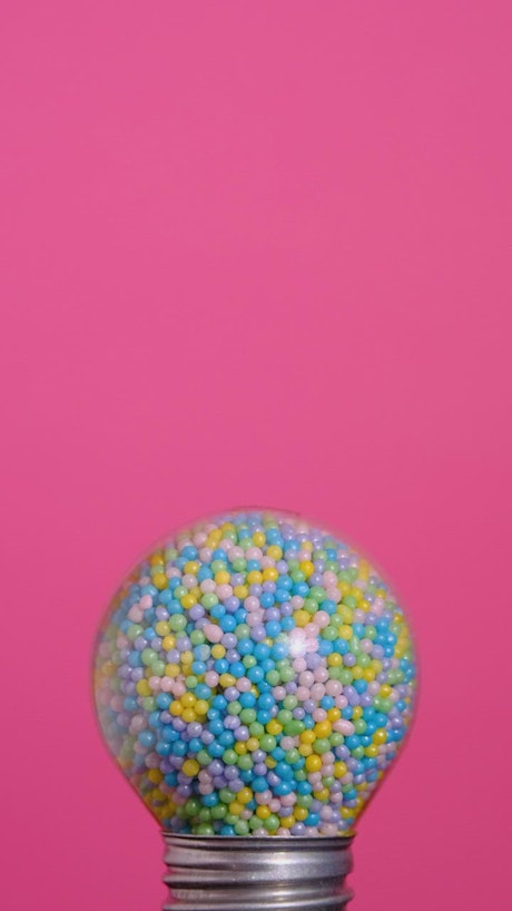 Round spotlight that glows full of colorful candies on a pink background.