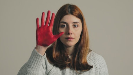 Sad girl raises her red painted right hand to stop the violence.