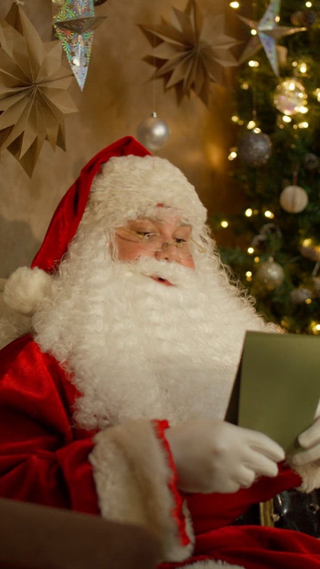 Santa Claus attentively reads a letter on green paper with shimmering christmas tree lights in the background.