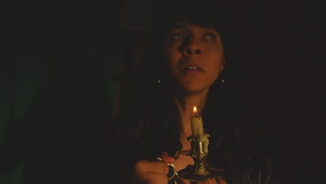 Scared woman in a dark place with a candle in her hand.