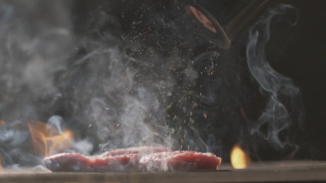 Seasoning a grilled steak on flames.