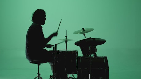 Shadow of a drummer playing on a green background.