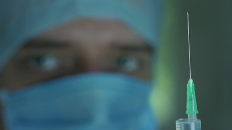 Shallow focus of a doctor looking at the syringe.