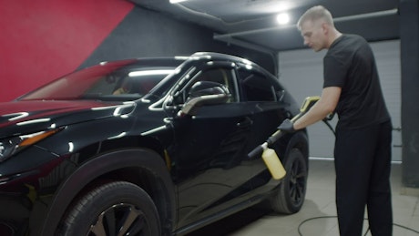 Shiny black car being sprayed with a cleaning solution.