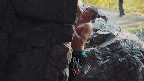 Shirtless man climbing a rock in the wild.