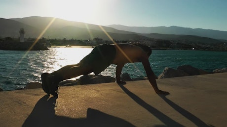 Shirtless man doing push ups on the boardwalk