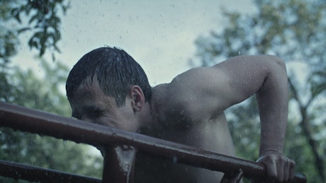 Shirtless man exercises in the rain.