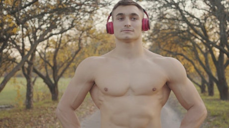 Shirtless man in headphones flexes muscles before outdoor workout