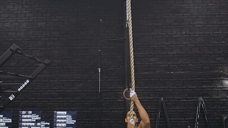Shirtless man rope climbing at the gym.