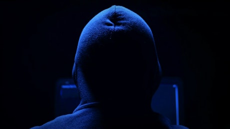 Shot from behind of a man in a hoodie working on his laptop.