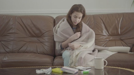 Sick girl on sofa checks thermometer for fever
