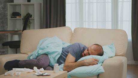 Sick man lays on sofa during coronavirus pandemic.