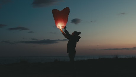 Silhouette of a boy holding a lantern in the countryside at sunset.