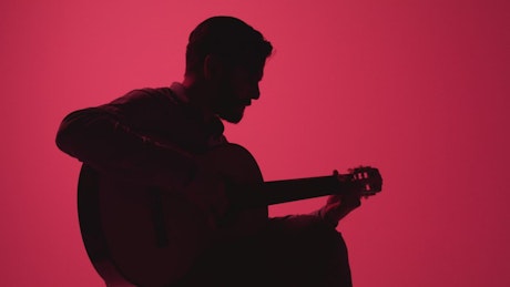 Silhouette of a guitarist playing on a pink background.